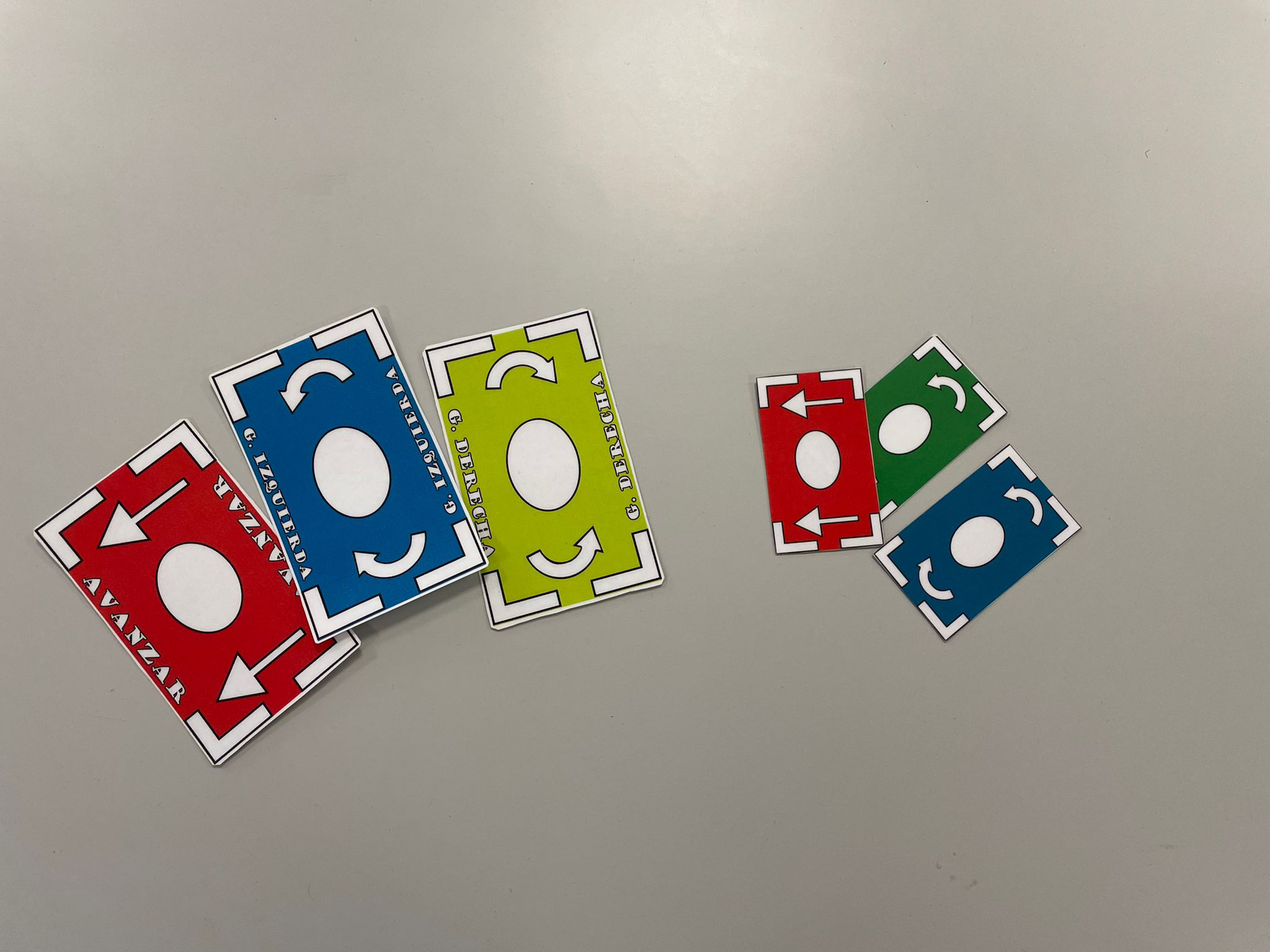 Image showing different types of cards, both initial and current versions. The current versions are a third larger than the first ones. From left to right, the current cards are displayed: Move Forward, Turn Left, and Turn Right. Then, the older versions follow, each one color-coded: red for Move Forward, blue for Turn Left, and green for Turn Right